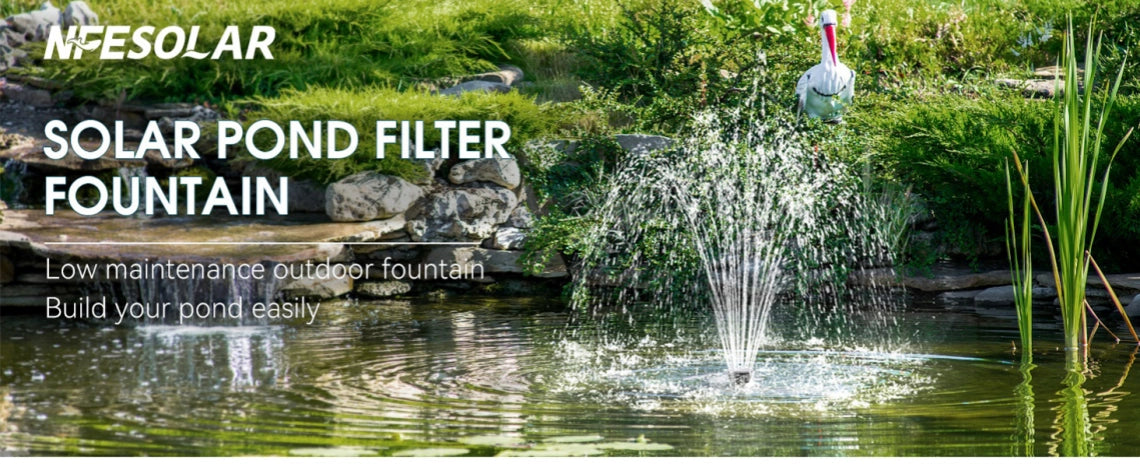 Solar-powered pond filter fountain spraying water in the center of a pond, with a backdrop of green plants and rocks, and a small waterfall.
